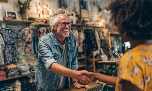 Smiling local shop owner shaking hands with a customer inside a Hampshire boutique, reflecting The Local Website Company&rsquo;s support for independent businesses.